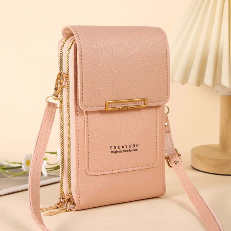 A light pink faux-leather crossbody phone pouch with gold-tone hardware, featuring a front pocket with the brand name 'ENDAYCON' printed on it, shown on a beige tabletop with a soft-focus background.